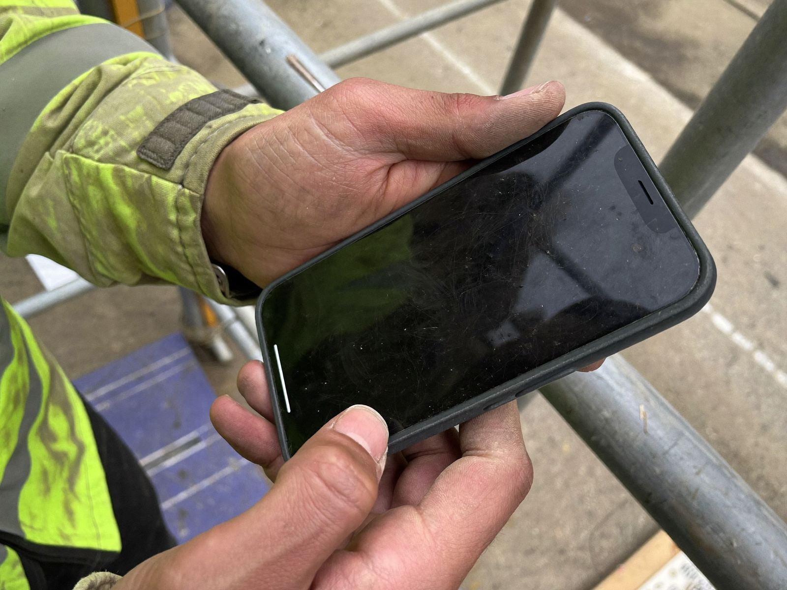 A builder's hands holding a phone on site